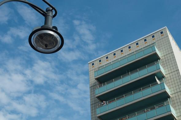 A lightly clouded sky with a highrise building in the background and a street lamp in the foreground.