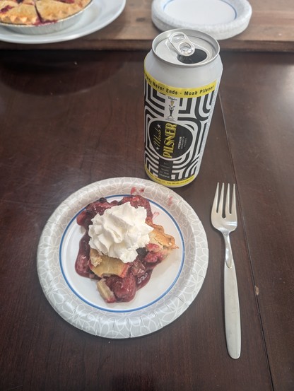 Photo of mixed berry pie on a paper plate with whipped cream on top. Next is an opened Moab Pilsner.