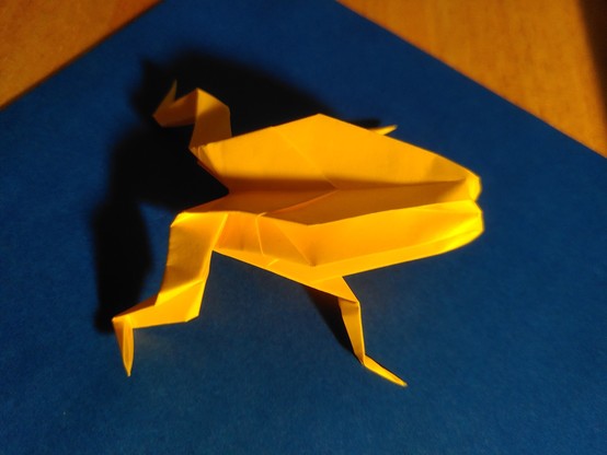 Une grenouille jaune en origami, avec quatre pattes fines et un corps en 3D mais avec une tête un peu bizarre (sans tête, en fait).