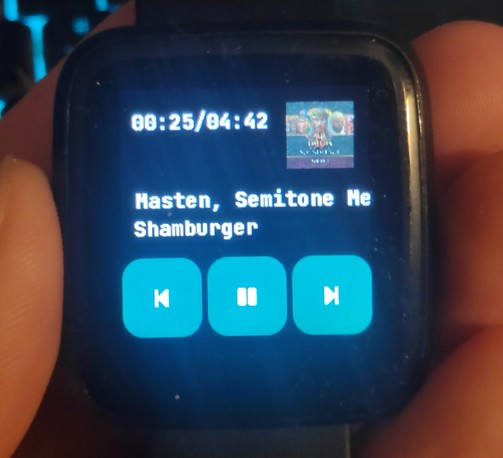 A Pinetime showing the music app of InfiniTime displaying music progress, artist, track, buttons for previous song, next song and pause and most importantly album cover. the track playing is Shamburger from Age of Empires 2.