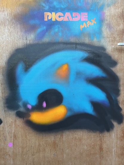 Graffiti of stylized blue cartoon character on a wooden surface with the text 