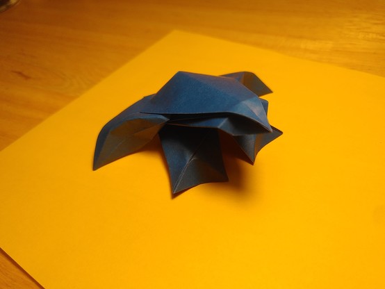Une grenouille bleue en origami. Elle a de grandes courbes, une tête très fine, peu de plis : elle est très simple mais très belle. Elle est de trois quarts.