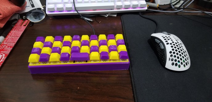 Photo of tiny 4x10 purple and yellow 3d printed keyboard on a desk next to a mouse that it longer than the keyboard is wide.