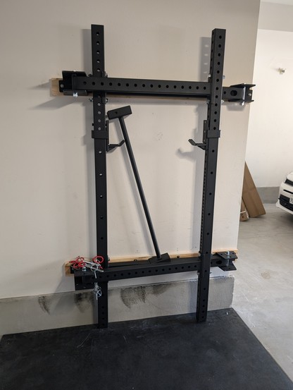 Folding squat rack, folded, against the wall of a garage from the front