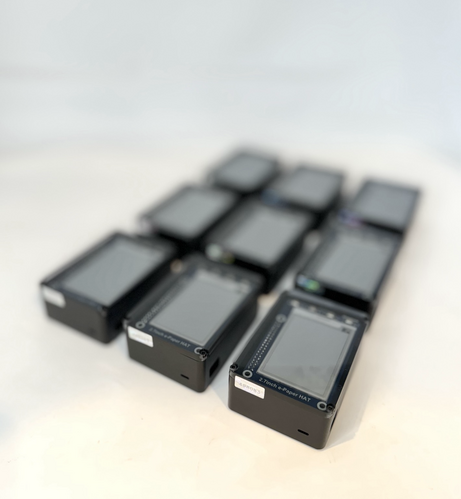 A set of nine Personal Server devices in a grid. The image shows blank epaper displays, and uniquely numbered tamper evident tags sealing the lid. 