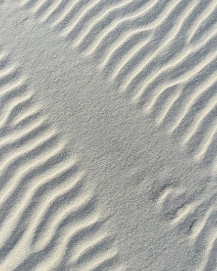 Ripples in white wind driven sand bisected by a smooth flat fan made by some unseen object blocking the wind. 