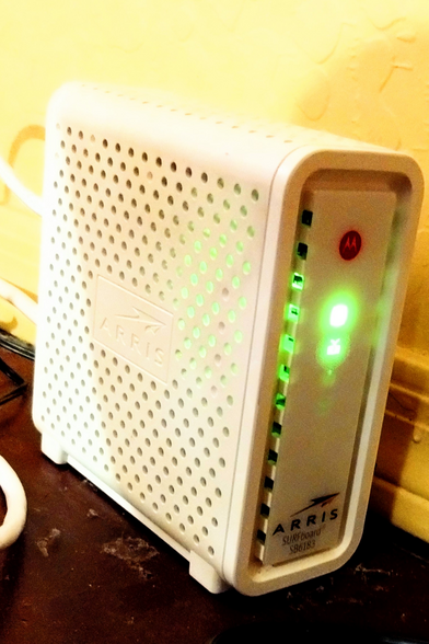 A white plastic rectangular cable internet modem. The display shows two green lights.