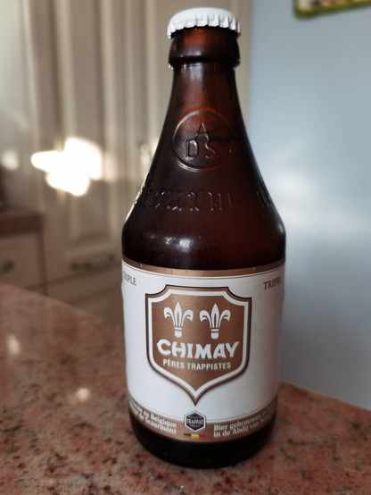 A stubby bottle of Chimay Tripel beer on a kitchen counter. It has a white and gold label.