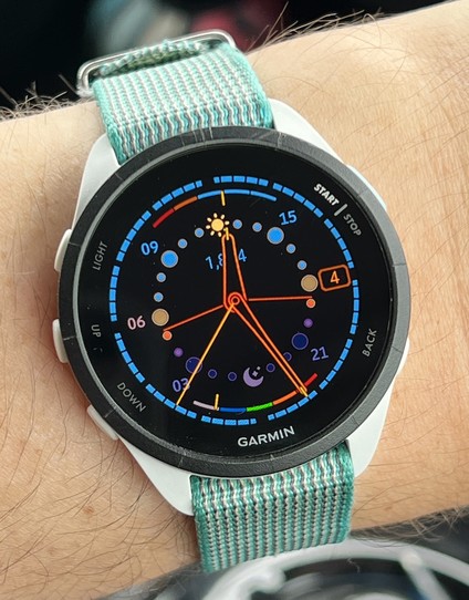 A smartwatch with a 24 hour dial, where the hour markers are on a smaller inner ring, and each one is coloured to show the approximate colour of the sky at that time of day. Noon and midnight are represented by a sun and moon icon respectively.

The outer minutes and seconds ring is coloured to match the current hour marker (sky blue, when this picture was taken), and there are two orange lines coming from the centre pointing to where on the hour ring the time of sunrise and sunset. At the top and bottom of the dial, just inside the minutes ring, are smaller arcs showing battery status and heart rate.

The time shown is 26 minutes and 37 seconds past noon.