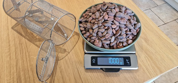 1kg of cocoa beans weighed out on the scales, next to the cage from our roaster.