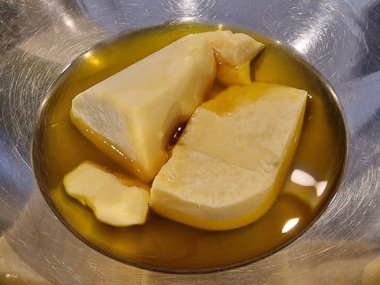 Top down view of some melting cocoa butter in a metal bowl (there's a pan of hot water underneath, out of view. Bain marie method)