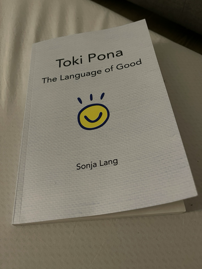The book “Toki Pona: The Language of Goof” by Sonja Lang lays on a white background. 