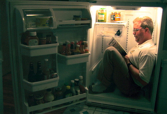 Man sitting inside a refrigerator reading a book.