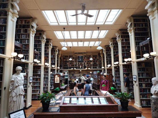 Photo of the interior of the library taken from the front entrance looking down the main hall. Two story bookshelves line both sides of the room.