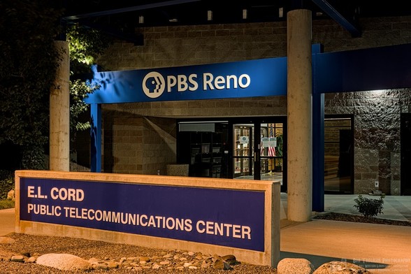 Color landscape photo of a commercial building front entrance area at night. A blue sign between two columns says, 