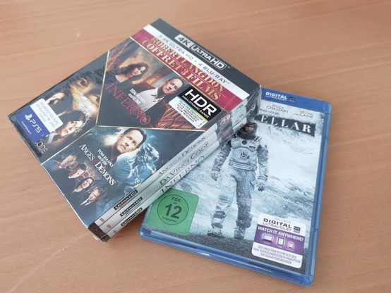 Blurays on a table. Interstellar on the bottom, and the 4k version of the Robert Lagdon trilogy partially on top. The latter is the French edition and is still shrinkwrapped.