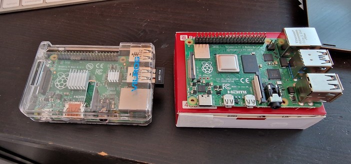 An original Pi B+ in a transparent case, next to a Pi4 B.