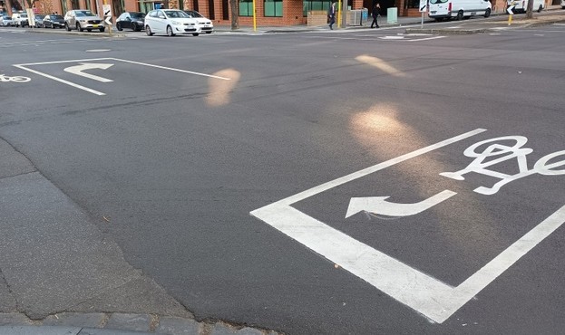 Road surface at an intersection with markings for cars to do a hook turn one way, and cycles to do a hook in another way.