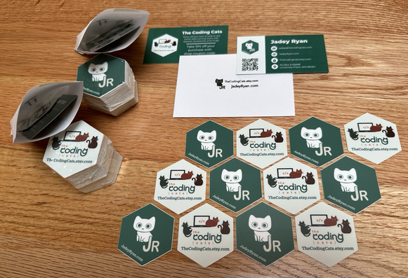 Jadey Ryan’s and The Coding Cat’s logos on hex stickers laid out with business cards and mini envelopes to collect more stickers!