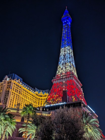 A half-scale replica of Eiffel Tower in Paris Las Vegas at nighttime. The tower is lighted in Blue, white, and red.
At the base is neon lights that says Paris Tower Restaurant