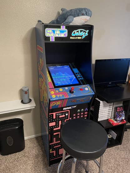 Arcade1Up Ms. Pac-Man/ Galaga cabinet playing Contra. On top of it rests a mini BLÅHAJ