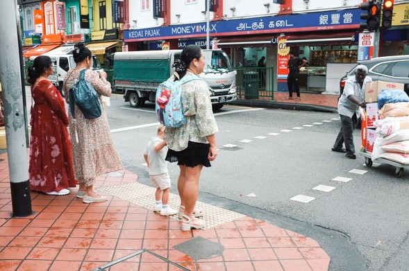 Pedestrians waiting at a traffic crossing, elderly Indian man pushing a trolley.