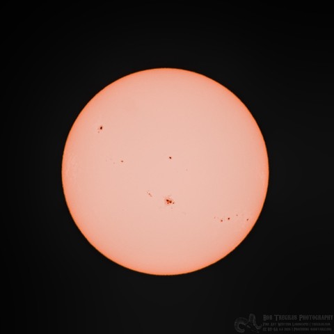 Color photo of the solar disk. It is light orange. There are about twenty black spots of various size on the disk, however, none are larger than a few percent of the overall disk.