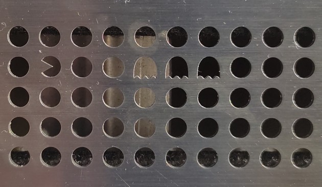 Metal grid with mostly circle holes but in the pattern there are 3 ghosts and pacman.