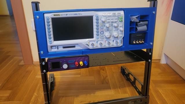 Rigol msp1074z oscilloscope mounted in a 3d printed rack mount. Additional storage space in the rack mount has a logic probe cable and a Red Pitaya device. It is mounted on a 19