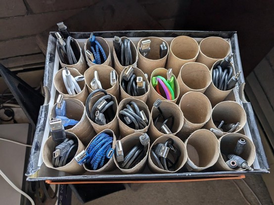 a shoebox full of cardboard rolls from toilet paper arranged vertically, each one containing a USB or audio cable so it's easy to see what each cable is