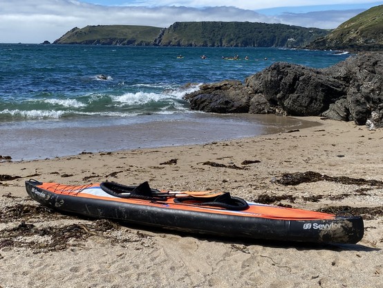 An orange inflatable double kayak on a sandy beach with white topped waves and blue sea and sky behind.