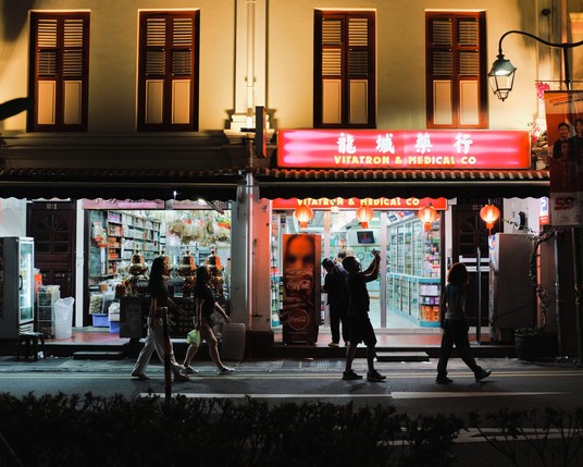 Night photo in front of a Chinese herbal medicine store in a row of shophouse with a few passerby one lifting his phone to take a photo.