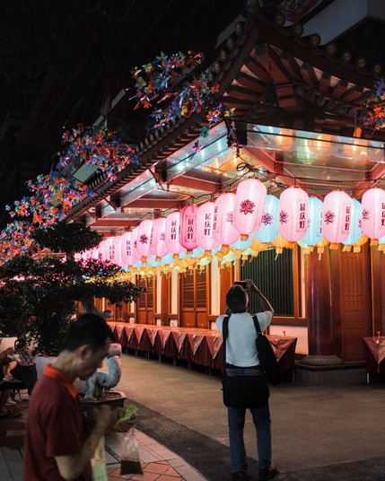 Visitor taking a photo of the lanterns decoration at a Chinese temple while another walking across with a packet of coffee in his hand.