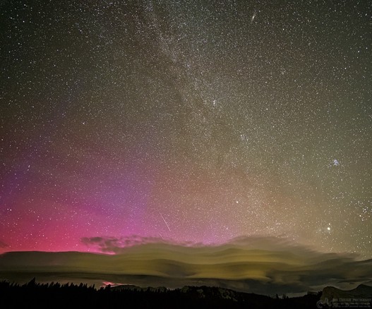 A color landscape photo of the night sky. The description in the post tells you pretty much what is seen here. With the exception that the landscape at the horizon shows the tops of conifer trees and large barren spots of granite mountain peaks. Oh, and the aurora on the left is red and purple and the clouds are a light yellow-green.