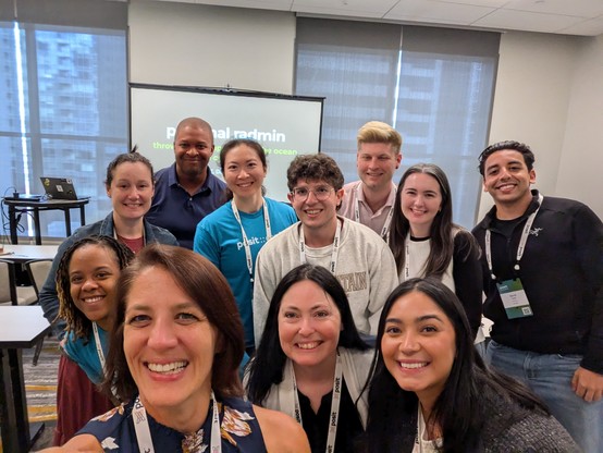 A group of 11 people taking a selfie in a hotel conference classroom.