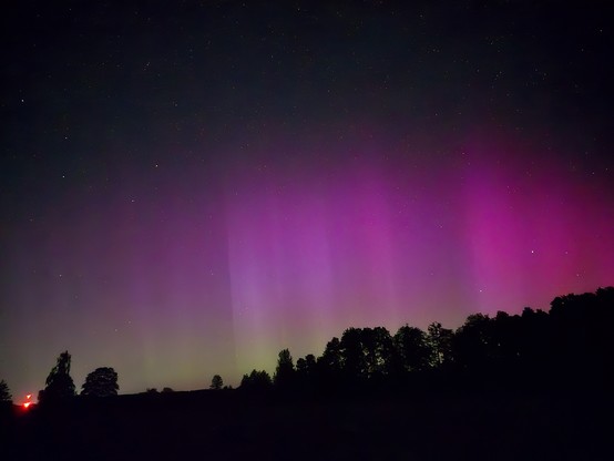 Aurola borealis or northen lights seen in the backdrop of a contryside night sky.