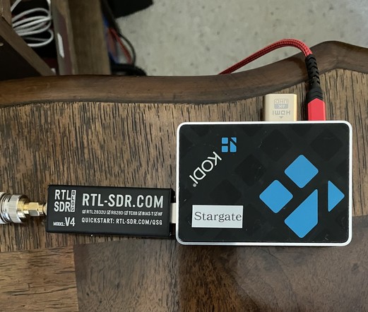 Picture of a RTL-SDR.com v4 dongle attached to a Pi 3 inside a black Kodi case with glue accents.