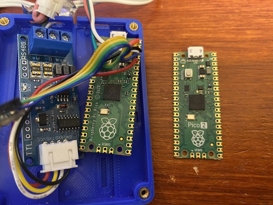 A case containing an RS-485 serial comms board and a Raspberry Pi Pico with soldered wires connected to it, alongside a Pico 2 board fresh out of the packet.