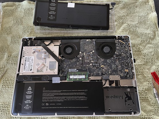 An opened laptop is shown, revealing its internal components. The old battery is detached and placed above the computer. The  ew battery is now installed. 