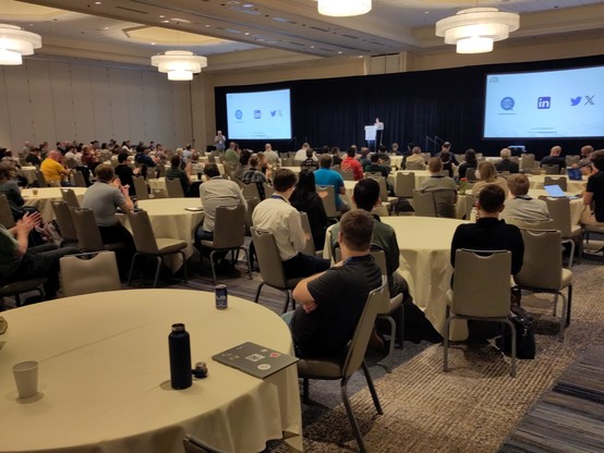 A large room with people watching a speaker on stage