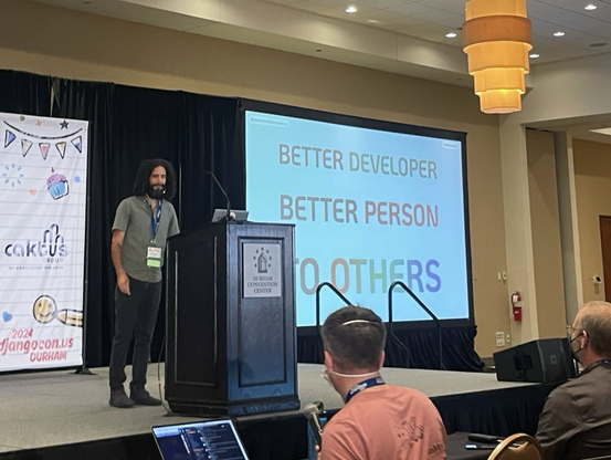 Mario at the podium in front of a slide that reads “Better Developer, Better Person, to Others”