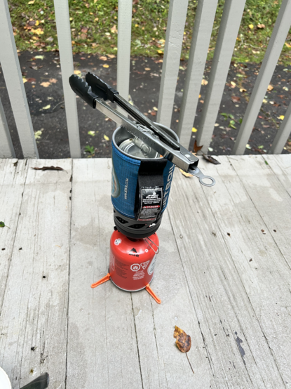 jet boil stove, with a soup can suspended from a pair of tongs while water boils around the soup