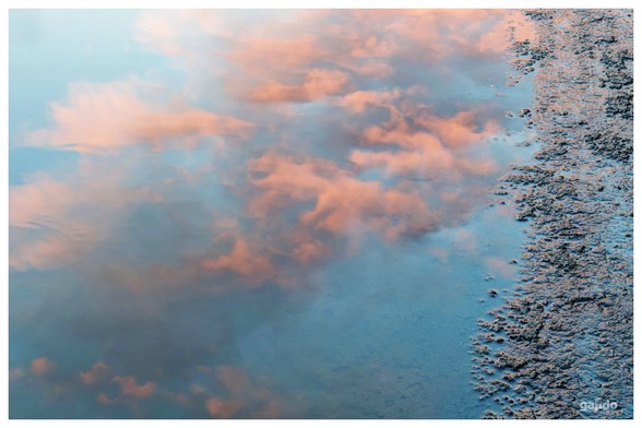 A pink morning sky reflected in a puddle of water