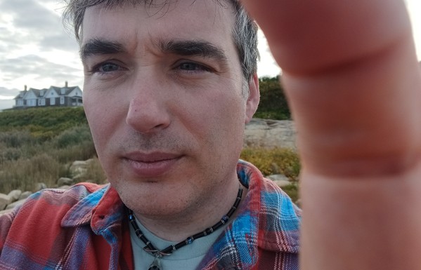 A big dumb man with sea oats and a house in the background 