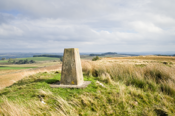 Concrete trig point on wild grassy moorland, under cloudy skies.