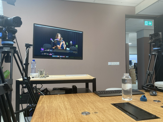 A photo of a podcasting studio. There are multiple cameras on tripods in the room. There’s a computer screen with a camera feed hat shows Judith van Stegeren sitting behind a podcasting microphone, taking a photo with her phone.