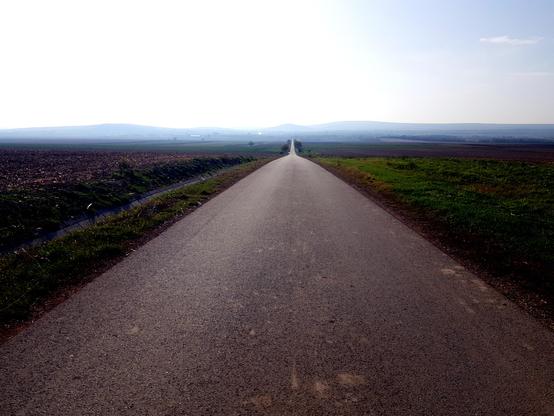 Budapest - Balaton cycle route. Very long straight road ahead descending a bit like in Arizona Death Walley. In the background there are some hills in the fog.
