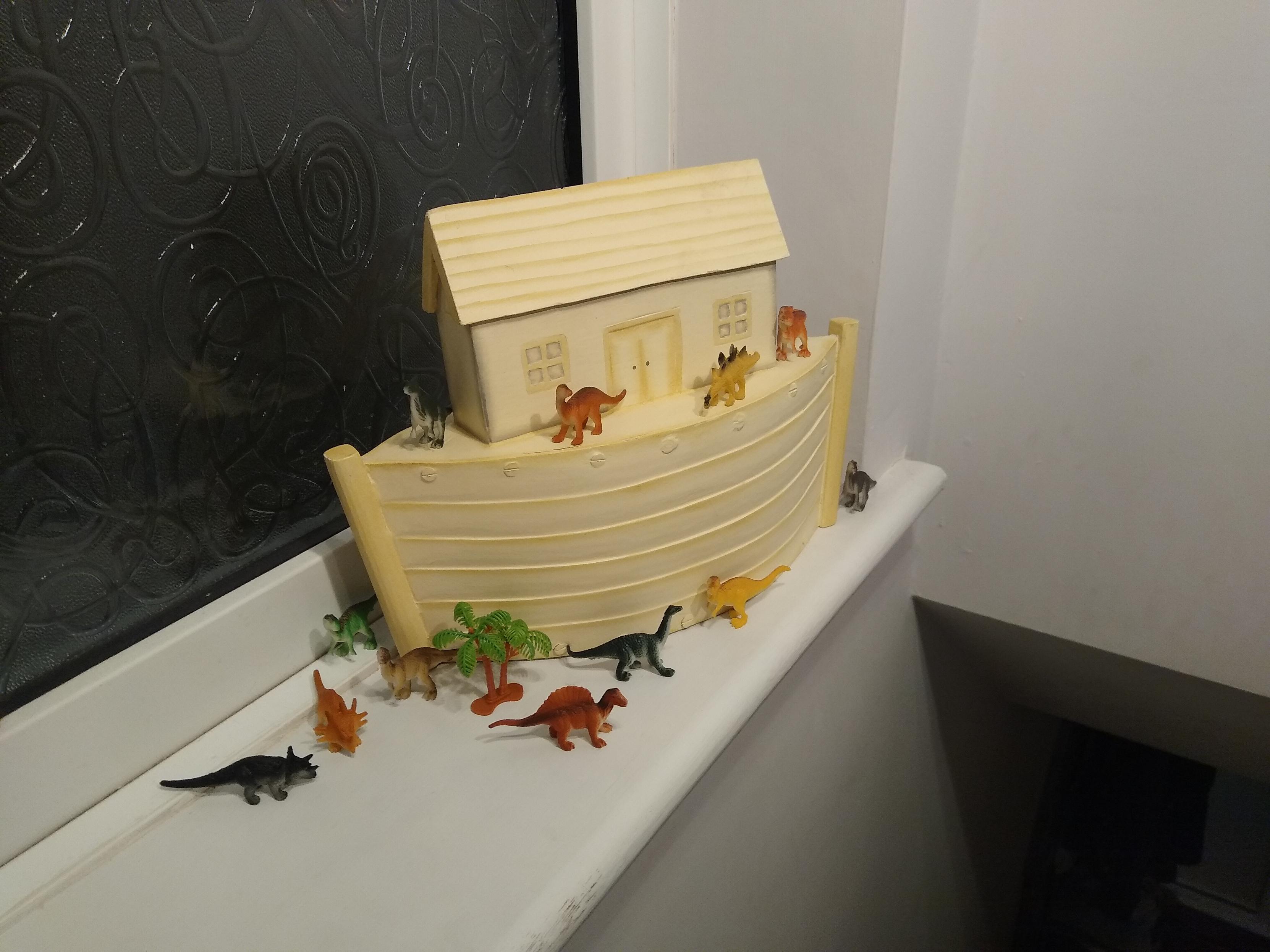 A wooden Noah's Ark model, looks like it was an old toy, and it appears to be inhabited by various small plastic dinosaurs.