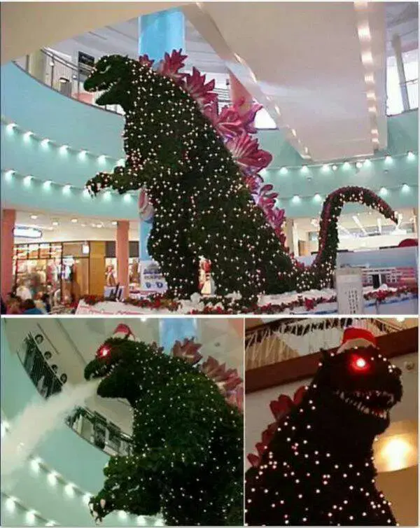 A festive Godzilla shaped Christmas tree spewing seasonal atomic breath towards what appears to be the interior of a shopping mall.