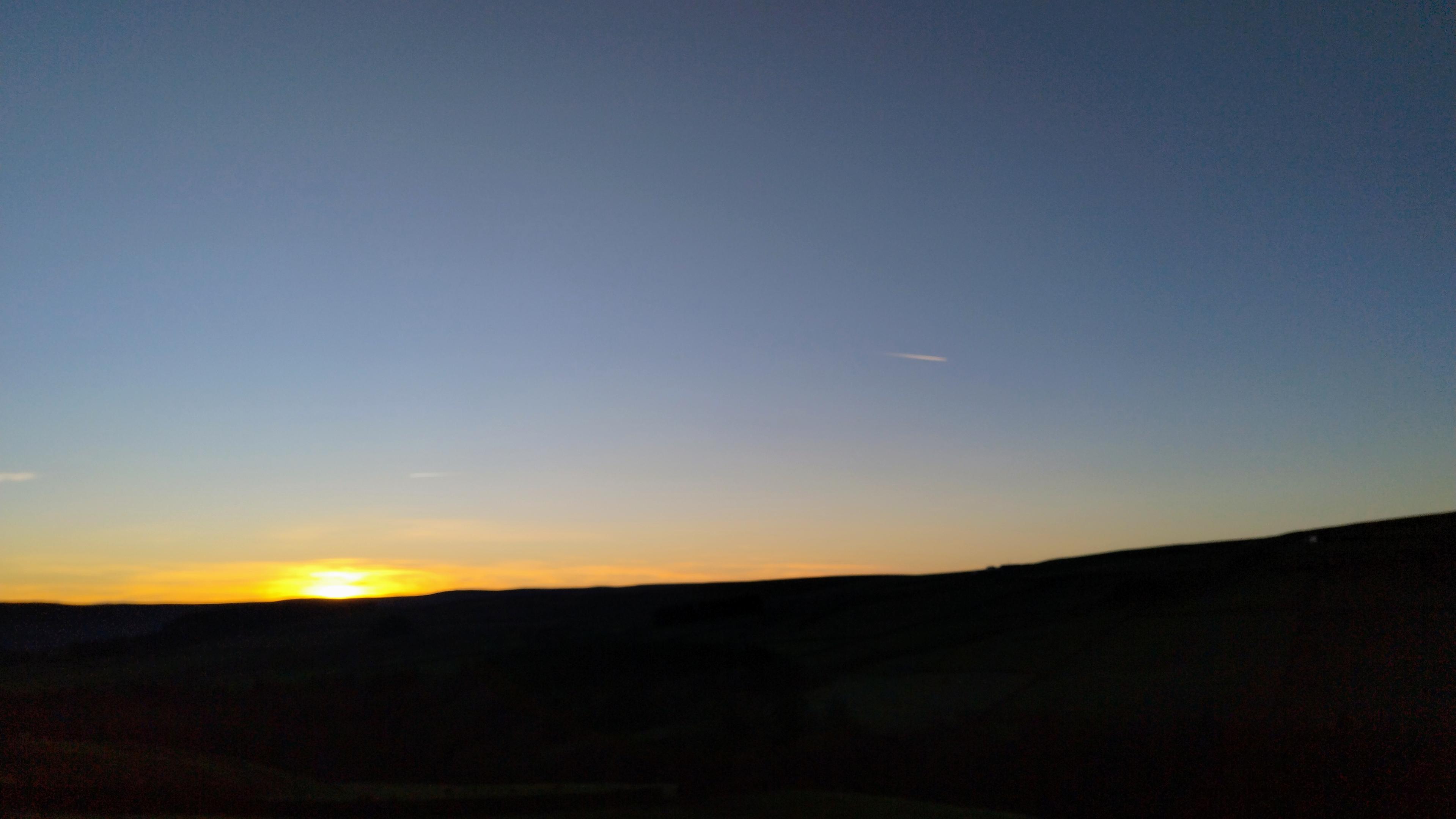 Sunset, with ground in silhouette and a clear sky fading from orange to dark blue.